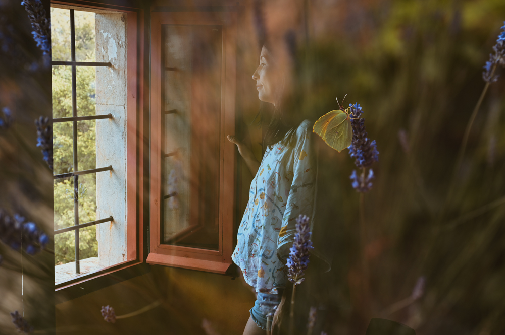 Frau steht träumerisch am Fenster mit Lavendel und Schmetterling – Frauenfotografie Mareen Zimmermann