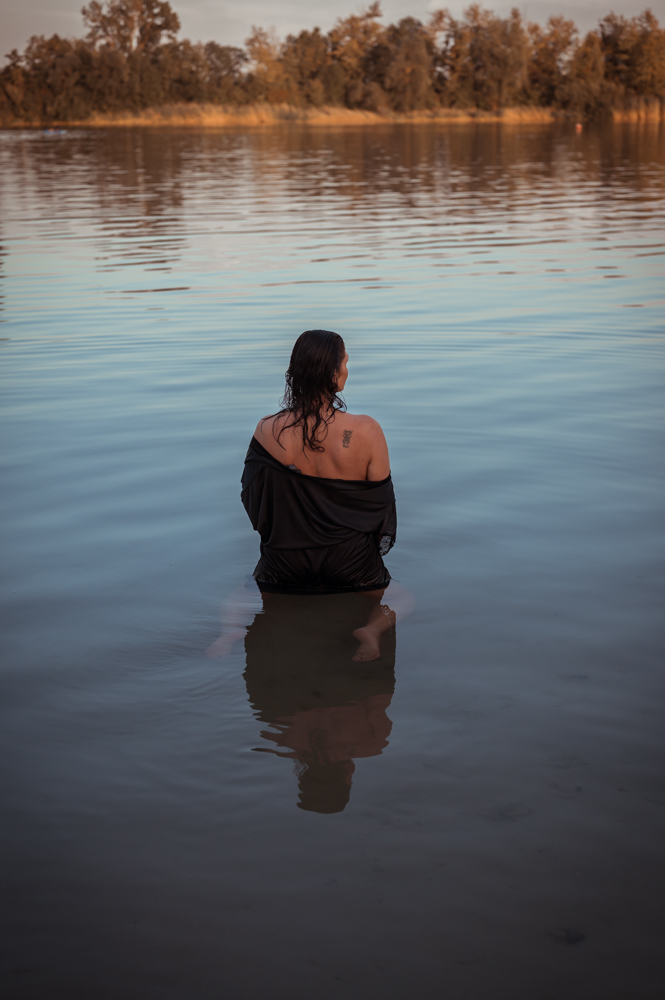 Frau von hinten im See, schwarzes Kleid, stille Wasseroberfläche mit Spiegelung – meditative Seelenfotografie von MALEA Fotografie