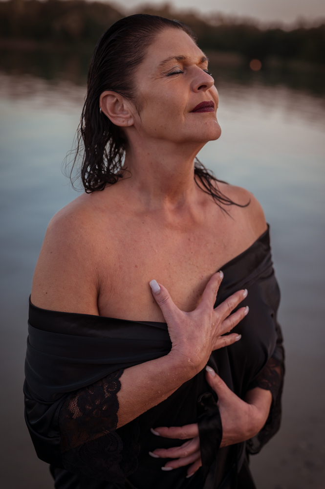 Frau im schwarzen Kleid am Wasser umarmt sich selbst, Augen geschlossen – intensive Seelenfotografie von MALEA Fotografie